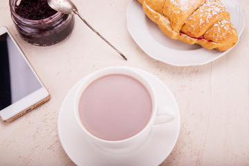 Fototapeta na wymiar Croissant with raspberry jam, cocoa in a mug, in hand mobile phone.