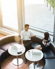Two asian coworkers use laptop work together having coffee in afternoon
