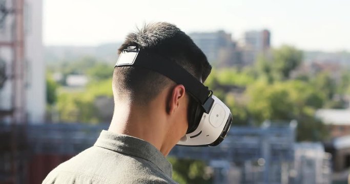 Closeup of Young man experiencing virtual reality through a VR headset on urban industrial background, summer 4k
