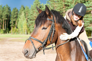 Girl equestrian riding horseback and stroking horse neck. Summertime outdoors