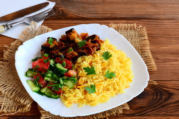 Roast vegetable risotto, stewed eggplants, salad with fresh tomatoes and cucumbers on a white plate and a wooden table. Summer vegetarian dish idea. Rustic style
