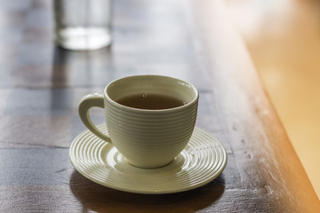 A glass of hot tea is on a brown wood table in a cafe.