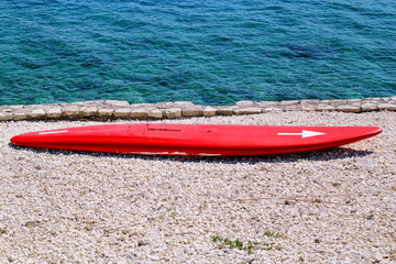 A red surfboard on the waves, on the beach by the sea. Beach landscape with surfboard on the sand. Surfboard on white sandy beach. Surfboard on the beach awaiting fun in the sun.