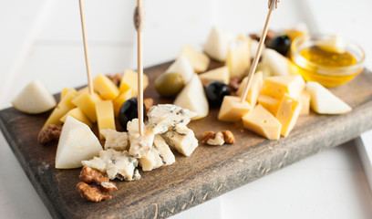 Assorted variety of cheese with honey and nuts. Placed on a dark wooden board