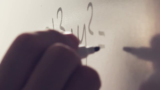 Math teacher writing mathematical formula on whiteboard in classroom, close up of hand with marker pen