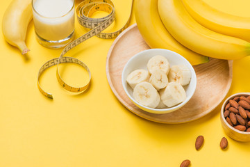 Bananas and almonds with measuring tape on yellow background with copy space