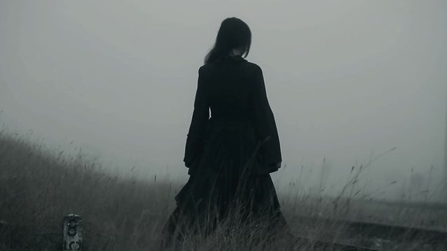 Horror scene of a scary woman in black dress walking away from camera