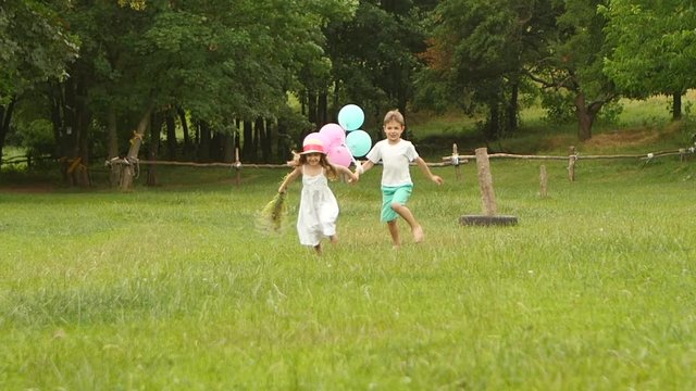 Little boy holds the girl by the hand and they run along the lawn together. Slow motion