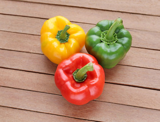 Green, red and yellow bell pepper on wood background.