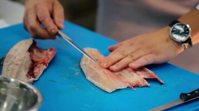 Close-up. The cook preparing the fish on the kitchen of the restaurant. Man cuts a knife fish bones in the fish fillet on the cutting board. Man puts the bones into a bowl.