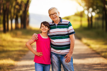 Obraz premium Portrait of happy grandfather and granddaughter standing in nature.