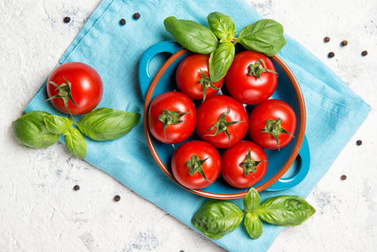 Fresh cherry tomatoes in a bowl, basil leaves and black pepper on stone table, closeup, top view