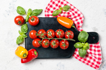 Ripe red cherry tomatoes with fresh basil leaves and colored baby bell peppers on a marble cutting board, top view