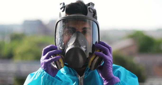 Chemical virus contamination concept, Firefighter Virologist chemical researcher young attractive man dressing gas mask avoiding deceasing of poisonous fumes, industrial factory city urban background