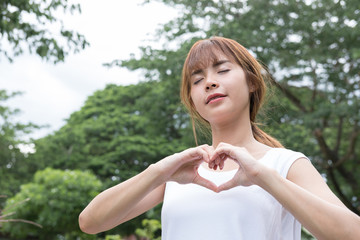 young woman making a heart gesture with her fingers. asian girl showing her love with hand sign in the park