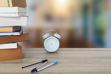 Books, textbooks,blue classic alarm clock and pens on vintage wooden table on blurred room background, business or education concept