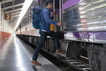 Obraz premium young man, tourist or traveler stepping up to the train on railway at train station. Travel, journey, trip concept