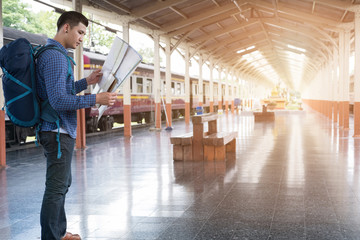 asian man with backpack standing on platform at train station. backpacker or traveler look at map while waiting for train. journey, trip, travel concept