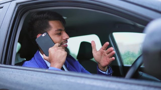 Modern arab man in formal wear sitting in right-hand drive car on the driver's seat and talking on cell phone