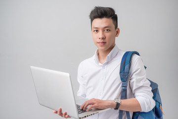 Happy casual asian male student using laptop isolated on a gray background