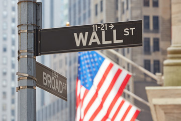 Wall Street sign near Stock Exchange with US flags, financial district in New York in a sunny day