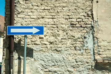 One way traffic road sign with grunge ruin brick abandoned house wall in background. 