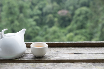 white tea in cup and mug on wood table with green nature background