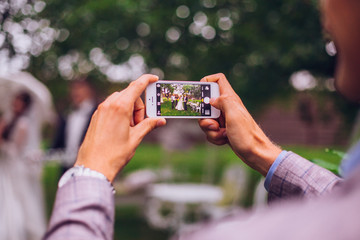 Man taking photo on phone of stylish wedding bride and groom posing. photo booth. wedding couple making photos with friends on phone camera. hand holding smartphone