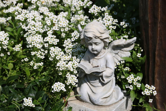 Engel auf einem Grab zwischen Blumen auf dem Friedhof