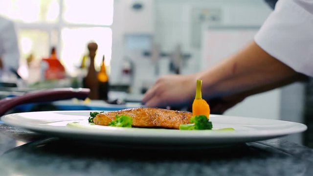 The cook decorating the fillet of fish on the plate. The man put the carrot on the plate near the fillet of fish.