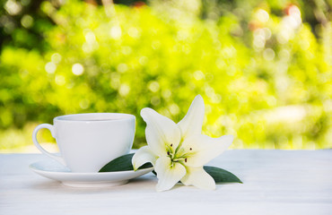 White coffee cup and white lily on the table. Purity and tenderness. Morning coffee in the garden. Copy space