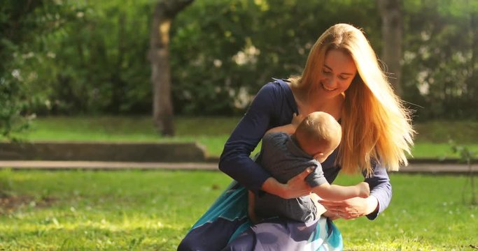 Portrait of happy little mom tenderly shaking son outdoors on green summer garden with fresh green grass background Cute european mother embracing baby boy 4k