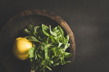 Fresh basil leaves and lemon on wooden plate over dark background. Top view with copy space, toned...
