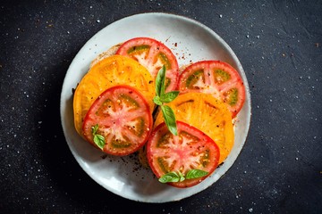 Tomatoes and basil garnished with crushed pepper and olive oil on sourdough bread on a plate. Dark background. Top view, closeup