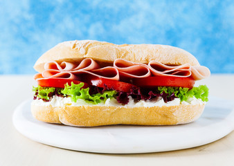 Italian healthy sandwich with tender ham, tomatoes, fresh lettuce leaves on a blue background.