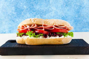 Italian healthy sandwich with tender ham, tomatoes, fresh lettuce leaves on a blue background.