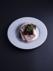 Danish open faced sandwich (smoerrebroed) with Danish cold cut made from pork (rullepoelse), aspic jelly (sky) and garden cress on dark rye bread. Placed on white plate on a black background.