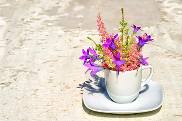 Astilba and blue bell flowers bouquet in a white coffee cup on an old white background with copy space for your text