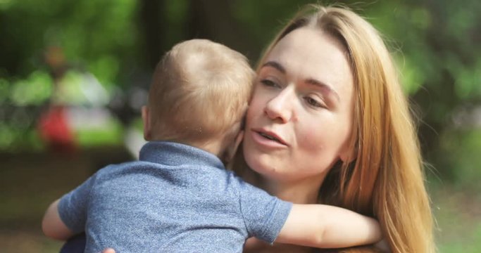 Mother with kid boy sitting on green grass and playing with her little son on summer sunset. Woman with children outdoors. Lifestyle concept 4k