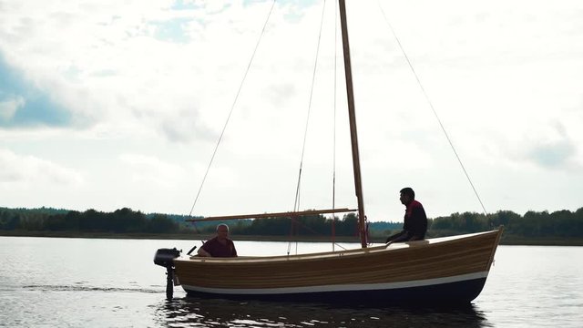 Mature Caucasian Master and his asian assistant working on wooden sailboat on river or lake. Smooth movement footage. They try to install mast.
