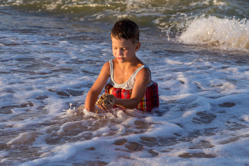 Fototapeta premium Little boy playing with sand in sea surf