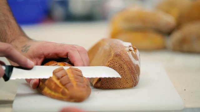 The cook cutting the bread at the table into three pieces. The man take away the pieces. Man check for the raw loaf.