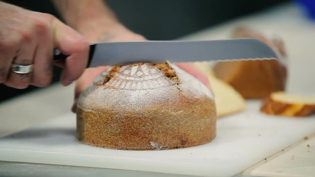 The man cut the bread into a two pieces. The man take away the pieces. Man check for the raw loaf.