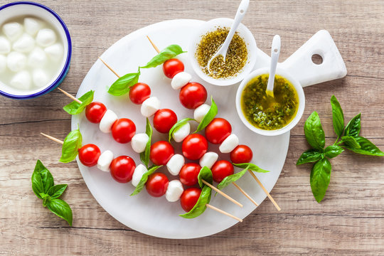 Appetizer in the form of caprese salad in the form of small shish kebabs for a summer healthy snack. On a wooden background