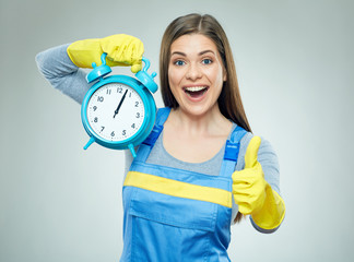 Smiling woman wearing builder overall holding alarm clock