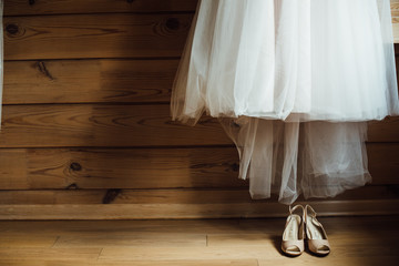 Fototapeta na wymiar bridal dress hanging on wooden wall next to the shoes