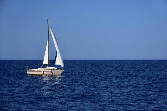 Peaceful afternoon, white sailboat at calm blue sea