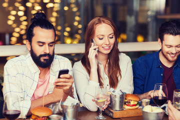 happy friends with smartphones at restaurant