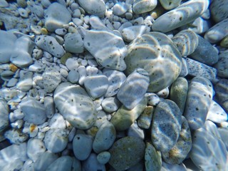 White pebbles underwater with the sun reflected in 