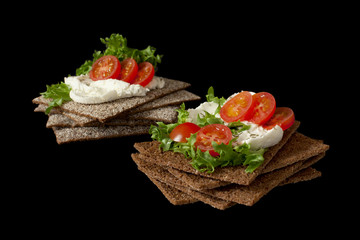 Healthy snack from wholegrain rye crispbread cracker with Cherry tomatoes, salad and soft cheese on black background